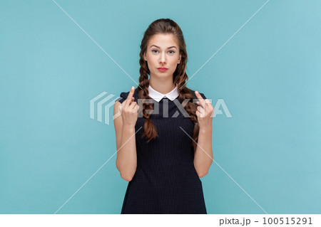 Portrait of serious vulgar woman with braids showing middle finger, impolite gesture disrespects someone looks rude at camera, wearing black dress. woman Indoor studio shot isolated on blue background 100515291