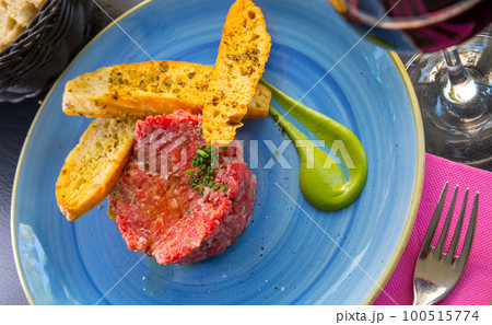 Picture of raw veal steak tartar served at blue plate with fried toasts Picture of raw veal steak tartar served at blue plate with fried toasts 100515774