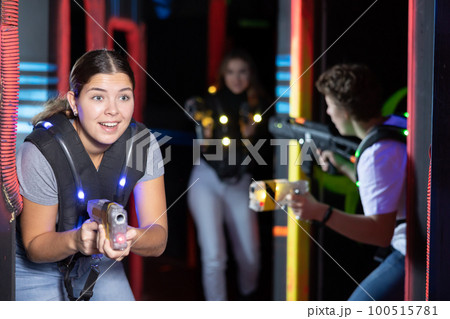 Smiling girl with laser pistol during playing laser tag with her friends in room Smiling girl with laser pistol during playing laser tag with her friends in room 100515781