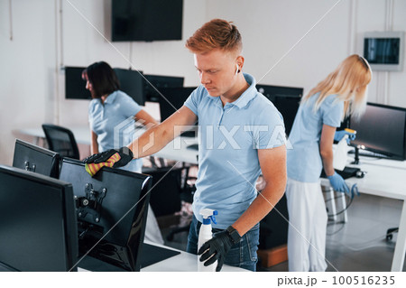 Cleans monitor. Group of workers clean modern office together at daytime 100516235