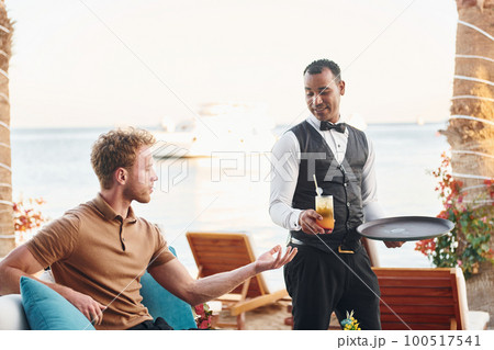 Serviced by waiter. Young man is outdoors at sunny daytime. Concept of vacation Serviced by waiter. Young man is outdoors at sunny daytime. Concept of vacation 100517541