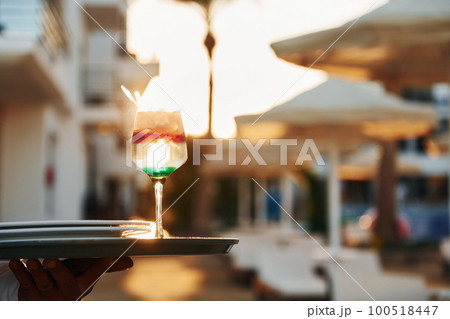 Close up view of drink. Black waiter in formal clothes is at his work outdoors at sunny daytime 100518447