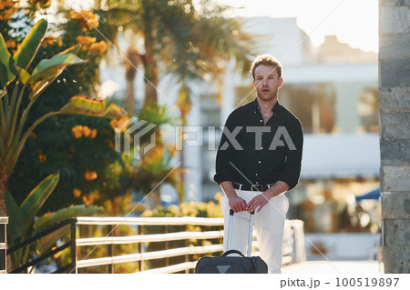 With travel bag. Young man is outdoors at sunny daytime. Concept of vacation 100519897