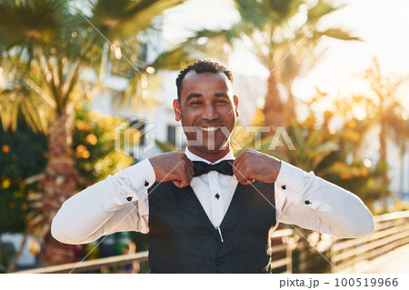 Posing for a camera. Black waiter in formal clothes is at his work outdoors at sunny daytime Posing for a camera. Black waiter in formal clothes is at his work outdoors at sunny daytime 100519966