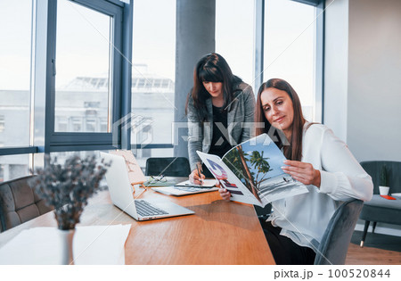 Two women in formal clothes is indoors in the modern office works together 100520844