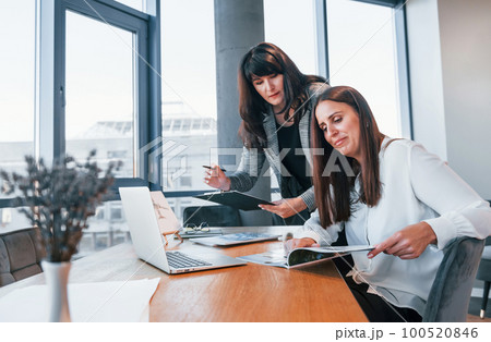 Two women in formal clothes is indoors in the modern office works together 100520846