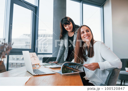 Two women in formal clothes is indoors in the modern office works together 100520847
