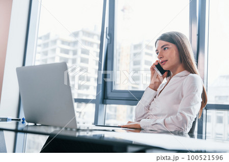 Busy day. Young woman in white formal clothes is indoors in the modern office Busy day. Young woman in white formal clothes is indoors in the modern office 100521596