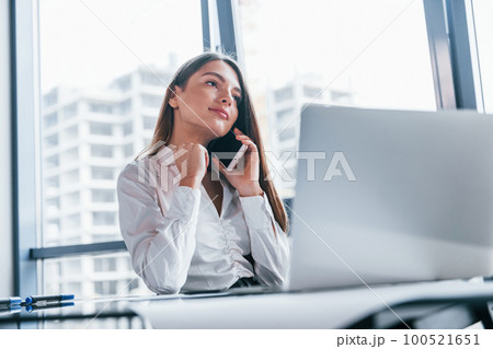 Young woman in white formal clothes is indoors in the modern office 100521651