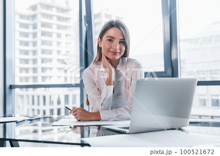 Young woman in white formal clothes is indoors in the modern office Young woman in white formal clothes is indoors in the modern office 100521672
