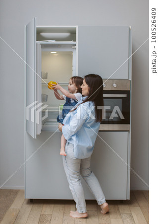 Mother holds a child in her arms and opens the refrigerator. Mother holds a child in her arms and opens the refrigerator. 100526409