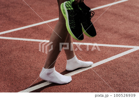 陸上競技場のトラックでフィニッシュ後シューズを脱いで歩く男性ランナー 陸上競技場のトラックでフィニッシュ後シューズを脱いで歩く男性ランナー 100526939