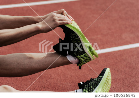 陸上競技場のトラックで脚をストレッチしてケアする男性ランナーの下半身 100526945