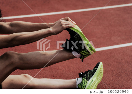 陸上競技場のトラックで脚をストレッチしてケアする男性ランナーの下半身 100526946