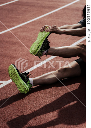 陸上競技場のトラックで脚をストレッチしてケアする男性ランナーの下半身 陸上競技場のトラックで脚をストレッチしてケアする男性ランナーの下半身 100526952