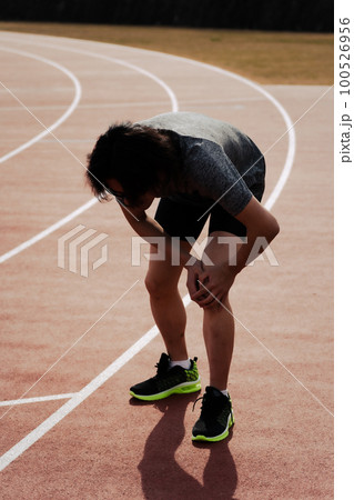 陸上競技場のトラックで膝をおさえてケアする男性ランナー 陸上競技場のトラックで膝をおさえてケアする男性ランナー 100526956