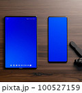 卓上に置かれたスマートフォンやタブレットを使って仕事をするビジネスマンの素材 100527159