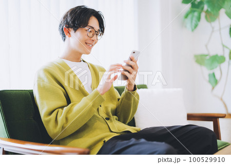 ソファに座ってスマホを使う男性 100529910