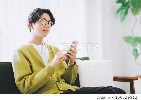 ソファに座ってスマホを使う男性 100529912