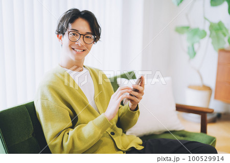 ソファに座ってスマホを使う男性 100529914