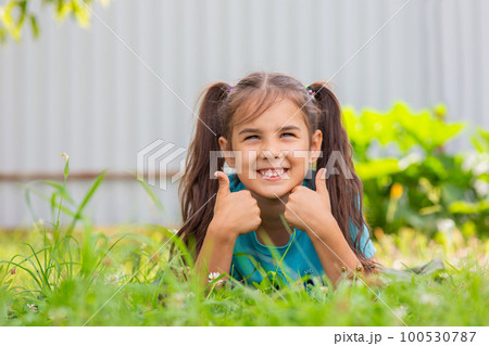 Cute smiling girl with lies on the green grass, in the summer garden 100530787
