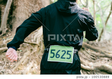 ゼッケンをつけてトレイルランニングする男性ランナーの後ろ姿 100530889