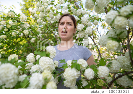 Unhappy woman with a clothespin on her nose on a walk in a blooming park.  100532012