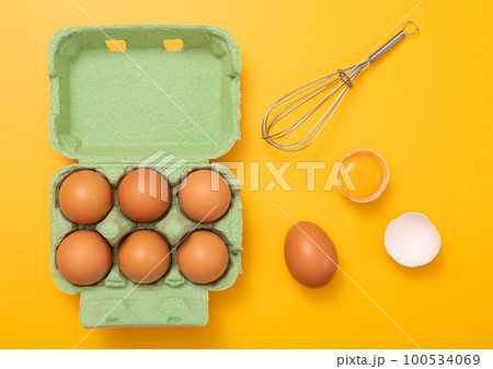 Green tray with organic brown eggs with yolk,whisk and shell on yellow.Top view cincept. 100534069