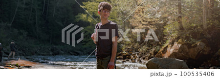 Young male traveler with backpack standing on rocks at river in mountains. Trekking route. Young male traveler with backpack standing on rocks at river in mountains. Trekking route. 100535406