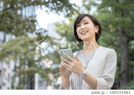 スマートフォンを持った笑顔の30代のビジネスウーマン スマートフォンを持った笑顔の30代のビジネスウーマン 100535963