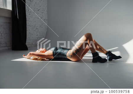 a sexy blonde with tattoos in a leather swimsuit and boots. a sexy blonde with tattoos in a leather swimsuit and boots. 100539758