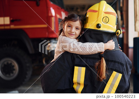 Happy little girl is with female firefighter in protective uniform Happy little girl is with female firefighter in protective uniform 100540223
