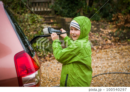 Happy child girl in waterproof clothes is helping parent washing car, water is splashing with sunlight Happy child girl in waterproof clothes is helping parent washing car, water is splashing with sunlight 100540297