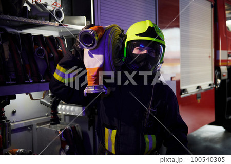 Holds hose. Male firefighter in protective uniform standing near truck Holds hose. Male firefighter in protective uniform standing near truck 100540305