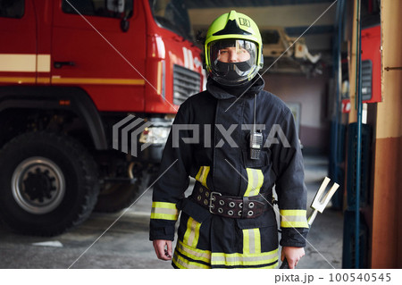 Male firefighter in protective uniform standing near truck Male firefighter in protective uniform standing near truck 100540545