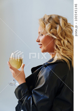 an attractive blonde in a black leather coat with a glass of champagne. an attractive blonde in a black leather coat with a glass of champagne. 100545146