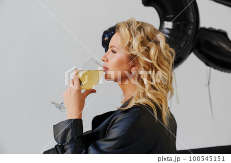 an attractive blonde in a black leather coat with a glass of champagne.  100545151
