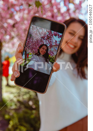 woman shooting her self on the phone under blooming sakura tree 100546027