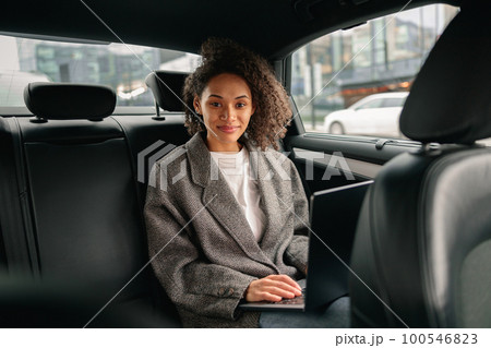 Smiling businesswoman manager working on laptop sitting car leather backseat on the way to office 100546823