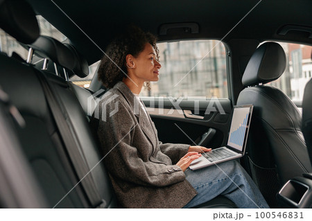 Executive woman sales manager working on laptop sitting car leather backseat on way to office 100546831