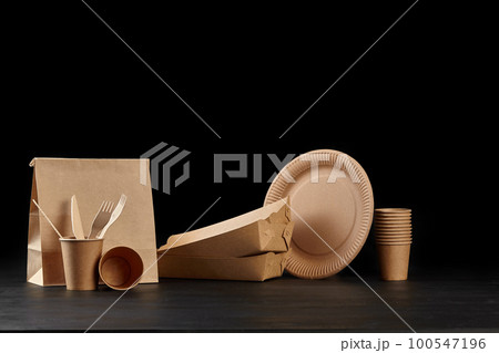 Eco friendly disposable tableware standing on dark surface against black background. Biodegradable craft dishes. Recycling concept. Close-up shot. 100547196