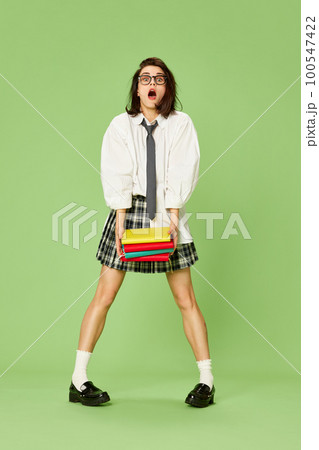 Young beautiful woman, student in checkered skirt and white shirt posing with books against green studio background Young beautiful woman, student in checkered skirt and white shirt posing with books against green studio background 100547422