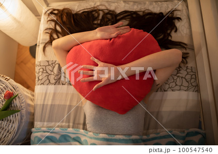 The red heart-shaped pillow is lying on the girls face. The red heart-shaped pillow is lying on the girls face. 100547540