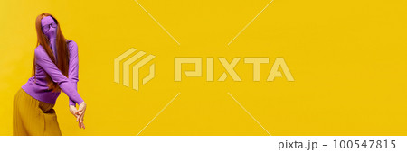 Faceless portrait of slim woman with long straight red hair wearing retro fashion outfit in action over yellow studio background. Impersonal emotions, body language 100547815