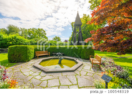 A small stone fountain with a statue and a wooden bell tower on Galarvarvskyrkogarden Cemetery in Stockholm, Sweden, on a sunny day 100548319