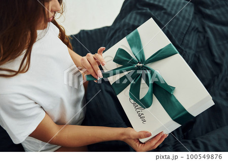 Gift box in hands of young woman. Interior and design of beautiful modern bedroom at daytime 100549876