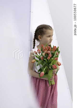 Adorable 9 years old girl with long curly hair walking through central square of the town Olesnica, Poland. Beautiful girl walking with bouquet of tulip flowers through spring European city. Adorable 9 years old girl with long curly hair walking through central square of the town Olesnica, Poland. Beautiful girl walking with bouquet of tulip flowers through spring European city. 100550677