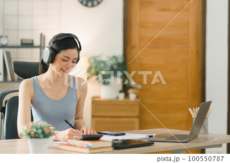 A beautiful young businesswoman is shown working on a laptop computer in her home office. The image represents the concept of working from home. A beautiful young businesswoman is shown working on a laptop computer in her home office. The image represents the concept of working from home. 100550787