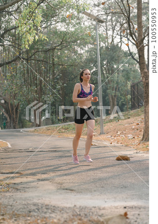 A beautiful sportswoman in sportswear is jogging outdoors in Autumn city park background. 100550953