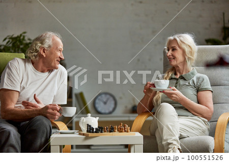 Happy elderly, senior couple, retired man and woman spending time at home, playing chess and talking together. Leisure time and hobby 100551526
